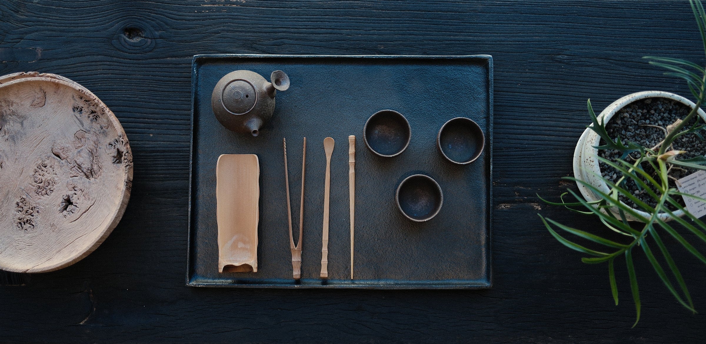 Tea set with teapot, cups, and utensils on a dark wooden tray.
